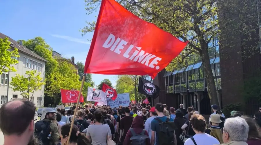 Rote Fahne mit Die Linke-Logo vor zahlreichen anderen Fahnen der 1. Mai-Demonstration in der Brunswicker Straße in Kiel.