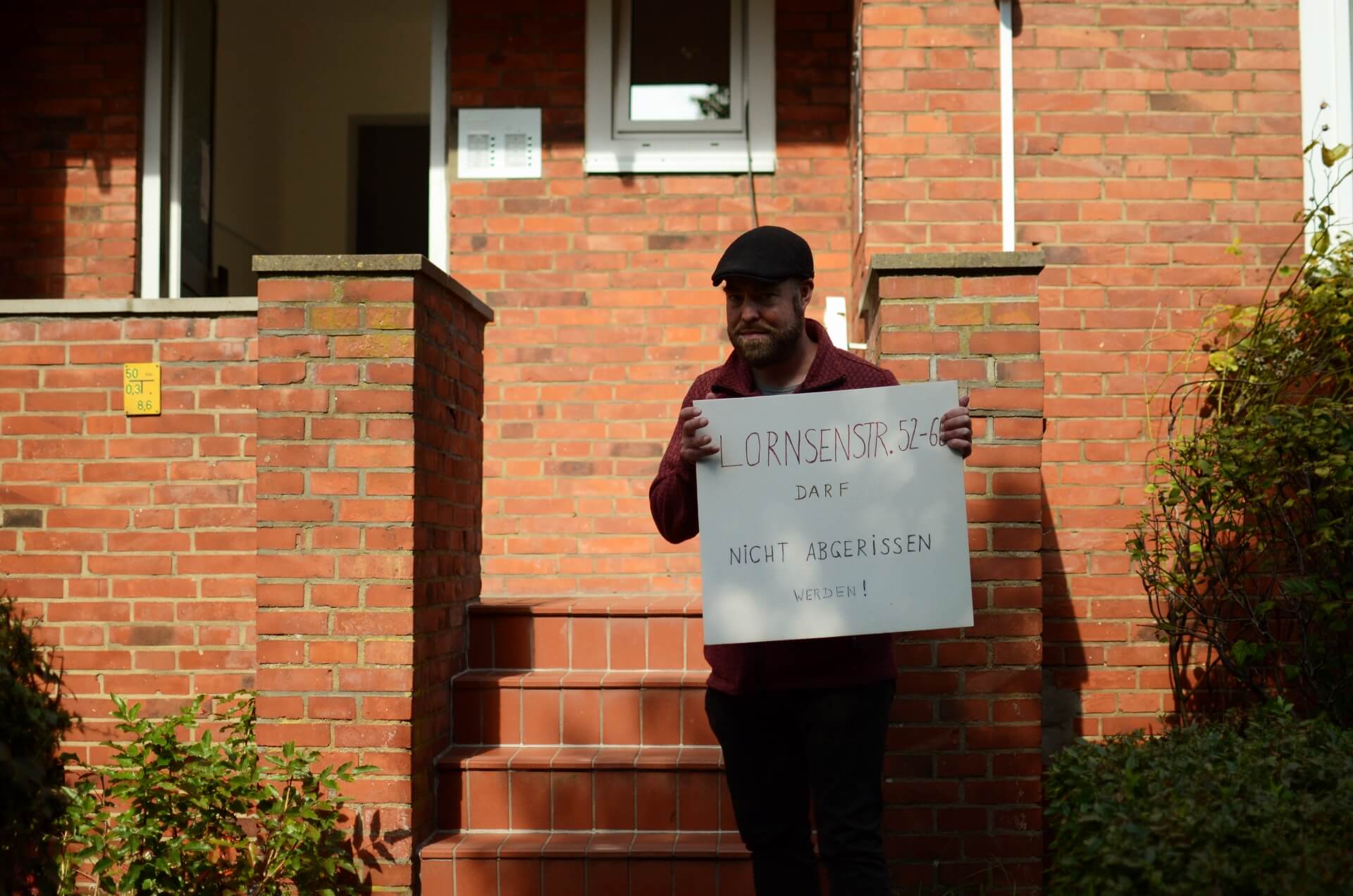 Björn Thoroe steht vor dem Zugang zu einem der betroffenen Miethäuser und hält ein Schild, auf dem steht: Lornsenstraße 52-60 darf nicht abgerissen werden!