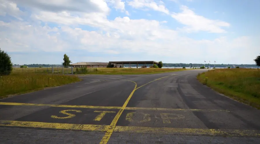 Ein Blick in Richtung Förde über das MFG5-Gelände. Im Vordergrund steht auf dem Asphalt der alten Hubschrauber-Rollbahn in großen, gelben Letter das Wort "STOP".
