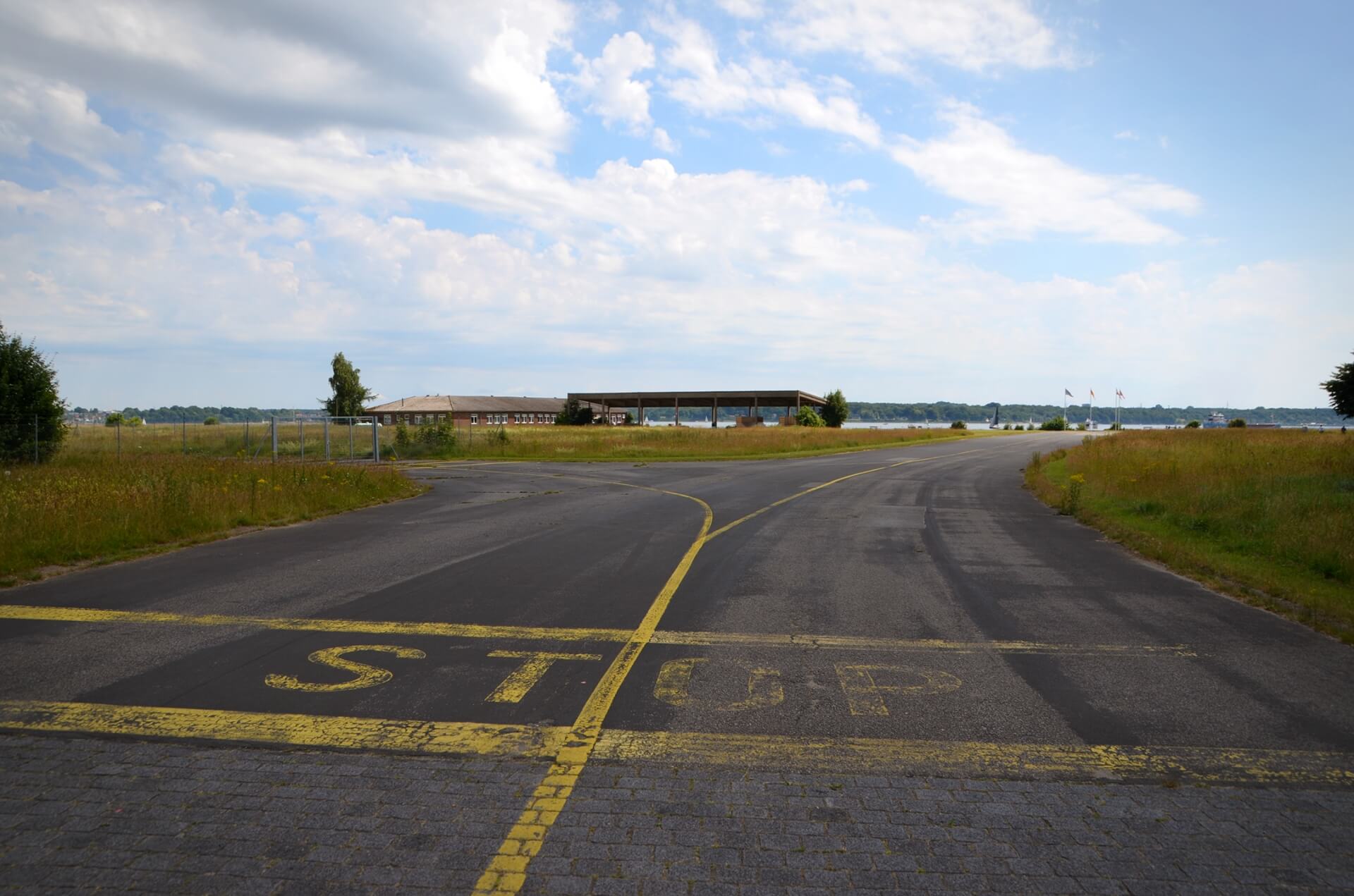 Ein Blick in Richtung Förde über das MFG5-Gelände. Im Vordergrund steht auf dem Asphalt der alten Hubschrauber-Rollbahn in großen, gelben Letter das Wort "STOP".
