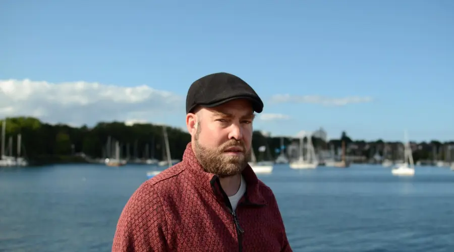 Foto eines grimmig schauenden Björn Thoroe. Im Hintergrund die Kieler Förde mit einigen Segelbooten.