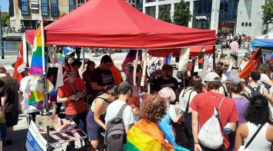 Zahlreiche Personen rund um einen Infostand von DIE LINKE und Linksjugend Solid auf dem CSD in Kiel.