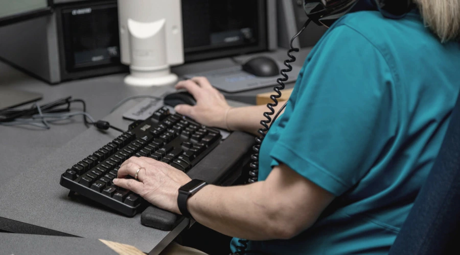 Eine Frau vor einer Tastatur, die sich ein Telefon zwischen Kopf und Schulter geklemmt hat.