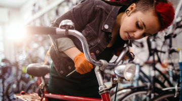 Eine junge Frau mit rot gefärbten Haaren repariert den Lenker eines roten Fahrrads.