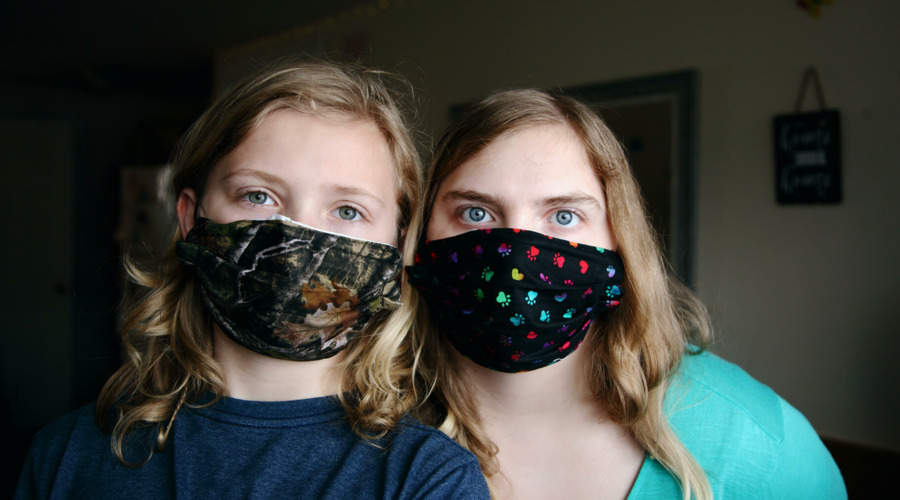 Ein Mädchen und eine junge Frau tragen bunte Masken zum Schutz vor einer Corona-Infektion.