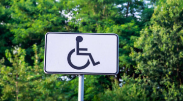 Ein Schild mit Rollstuhl-Piktogramm vor einem bewaldeten Hintergrund.