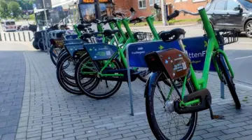 Eine Station des Bike-Sharing-Systems "Sprottenflotte" mit zahlreichen Leihrädern. Im Hintergrund die Alte Lübecker Chaussee in Kiel, mit Straßenverkehr und einem vorbeifahrendem Bus der Linie 42.
