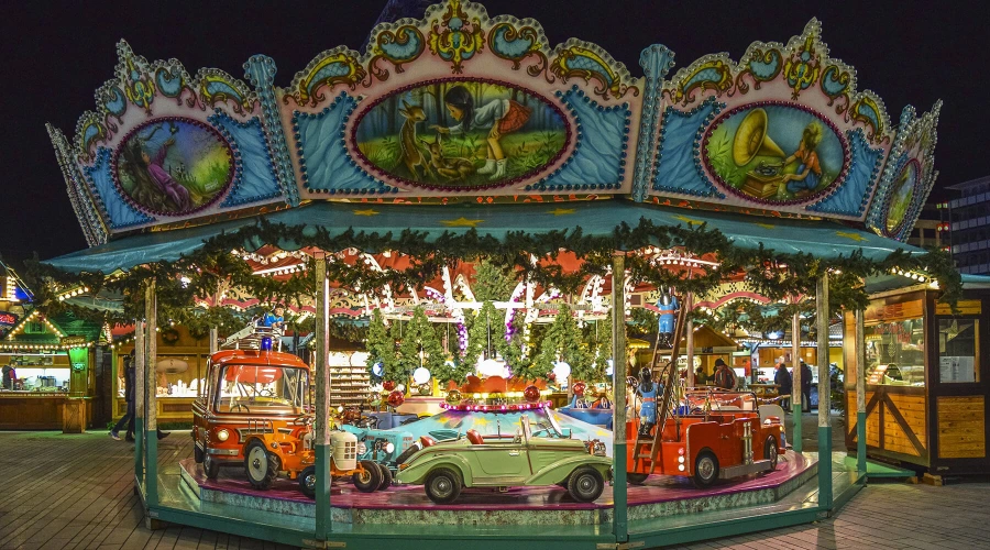 Ein weihnachtlich geschmücktes Kinder-Karussell mit verschiedenen Fahrzeugen, darunter Feuerwehr-Gerätewagen, auf einem Weihnachtsmarkt.