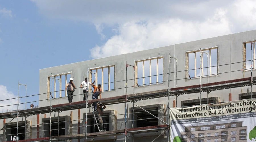 Bauarbeiter auf einem Gerüst vor einem im Bau befindlichem Wohngebäude.